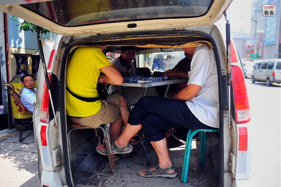 A group of road side vendors are playing Mahjong in a minivan to escape the heat of afternoon sun during their break.